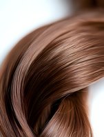 Close-up view of smooth flowing brown hair strands creating elegant curves and waves against white background, showing natural shine and texture.
