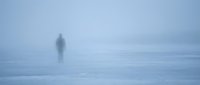 Solitary figure standing on frozen landscape in heavy fog and mist, creating atmospheric winter scene suitable for conceptual, editorial, and psychological storytelling projects.