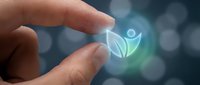 Person holding glowing holographic wellness icon with leaf and human figure symbol, representing health technology, digital medicine, and sustainable healthcare innovation.