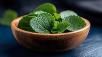 Fresh green mint leaves in wooden bowl on dark background, aromatic herbs for cooking, cocktails and tea preparation, selective focus macro photography.