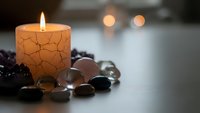 Burning candle with cracked texture surrounded by smooth stones creates peaceful spa atmosphere for relaxation and meditation practices.
