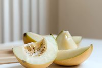 Fresh honeydew melon slices showing juicy flesh and seeds on white surface, soft natural lighting creates appetizing food composition for healthy eating concept.