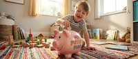 Young boy, Caucasian, approximately 5-8 years old, inserting coin into piggy bank while sitting on colorful rug in bright playroom. Educational financial literacy concept for children's savings and money management.