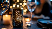Elegant perforated metal candle holder creates warm ambient lighting for romantic dinner table setting with wine glasses and festive bokeh background.