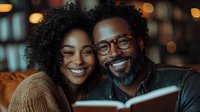 African American couple reading book together, sharing intimate moment with genuine smiles. Warm lighting creates cozy atmosphere for romantic evening at home.