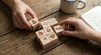 Hands arranging wooden blocks with eco-friendly symbols on rustic table with coffee cup and notebook for sustainable business planning.