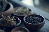 Assorted dried tea leaves in traditional clay bowls on wooden surface, moody atmospheric lighting creates depth and texture in dark tones.