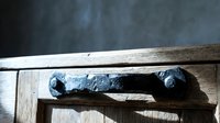 Rustic wooden door with aged wrought iron handle, textured weathered wood surface in soft natural light, vintage architecture detail.