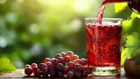 Fresh red grape juice being poured into glass with cluster of ripe grapes on wooden table in sunny vineyard setting for healthy lifestyle concepts.