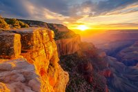 Dramatic sunset over Grand Canyon with golden light illuminating red rock formations and deep ravines against colorful sky.