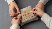 Hands exchanging eco-friendly mail package with sustainable shipping label, demonstrating green delivery and environmentally conscious postal service.