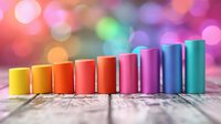 Colorful cylindrical tubes arranged in rainbow spectrum on wooden surface with vibrant bokeh lights background for creative design projects.