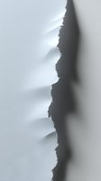 Torn white paper edge creating dramatic shadow and depth effect against dark background, revealing layered texture and jagged irregular pattern.