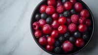 Fresh mixed berries in black bowl on marble surface featuring cranberries blackberries raspberries for healthy eating and cooking recipes.