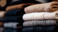 Neatly folded stack of cozy knitted sweaters in neutral colors from white to black creating gradient effect. Warm winter clothing arrangement for fashion retail.