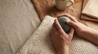 Woman hands holding green ceramic mug with hot beverage on cozy knit blanket. Relaxing morning coffee break at home with warm atmosphere and comfort.