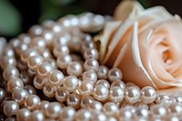Elegant pearl necklace with soft peach rose in background, macro shot highlighting lustrous surface and delicate details of luxury jewelry accessories.