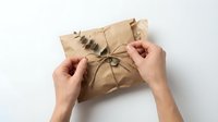 Hands unwrapping kraft paper package tied with twine on white background, gift opening, unboxing, delivery concept.