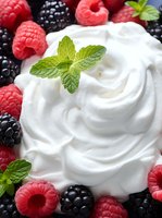 Fresh whipped cream swirls decorated with ripe raspberries, blackberries and mint leaves create an appetizing dessert composition for food photography and menu design.