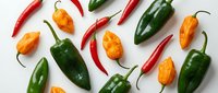 Colorful hot chili peppers scattered on white background. Fresh spicy vegetables including red cayenne, green jalapeno and orange habanero peppers isolated for cooking design.