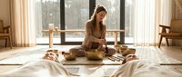 Woman in brown sweater arranging woven baskets and natural materials on floor near large windows in minimalist home interior space for lifestyle and home decor.