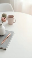 Minimalist workspace with pink mug, fresh pink rose in white vase, gray notebook and rose gold pen on clean white desk. Ideal for business, lifestyle and productivity content.