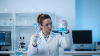 Female scientist in white lab coat examining blue liquid in test tube while holding DNA model in modern laboratory for research and biotechnology studies.