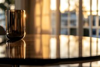Glass of red wine on polished dark table surface reflecting warm evening sunlight through window, creating atmospheric mood with golden bokeh effect.