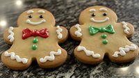 Festive gingerbread men cookies decorated with white icing, colorful bow ties and buttons on dark granite counter with twinkling holiday lights in background.