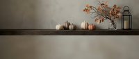 Autumn home decor with white and orange pumpkins on wooden shelf against neutral wall with dried branches and black lantern for seasonal interior design.