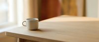 Minimalist workspace with steaming mug on wooden desk near window, conveying calm morning routine and productive work environment for office and lifestyle content.