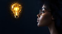 Young African American woman in glasses gazing at glowing magical light bulb floating in dark space, symbolizing innovation, creativity and bright ideas.