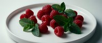 Fresh red raspberries with mint leaves arranged on a white plate, perfect for food photography, culinary content, healthy eating, dessert styling, and recipe illustrations.