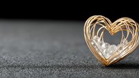 Golden heart-shaped light trails on dark textured surface creating romantic Valentine's Day concept with warm glowing lines and copy space for design.