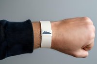 Close-up of male hand wearing dark navy sleeve and white wristband against neutral gray background. Caucasian adult arm extended in fist gesture. Suitable for business, fitness, motivation, and promotional campaigns.