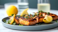 Grilled salmon fillets with charred marks, garnished with fresh herbs and lemon wedges on gray ceramic plate. Healthy seafood dinner with vibrant colors.