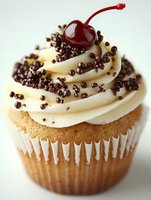 Vanilla cupcake with cream frosting topped with chocolate sprinkles and maraschino cherry on white background isolated for bakery menu design.