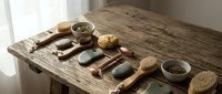 Spa wellness accessories arranged on rustic wooden table including natural soap bars, brushes, pumice stones and herbs in bowls for relaxation.