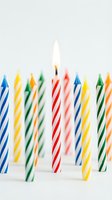 Colorful striped birthday candles with one lit red candle glowing against a white background, celebrating joy and festive party moments.