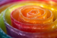 Vibrant spiral pattern of colorful candy with orange, red, yellow and purple stripes creating mesmerizing swirl texture in extreme macro photography.