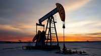 Oil pump jack silhouette against dramatic orange sunset sky, industrial equipment on winter field with snow, energy production site in dusk light creates moody atmosphere.