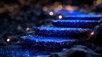 Sparkling blue glitter scattered on dark surface with warm bokeh lights creating magical atmosphere for luxury cosmetics and party decorations.
