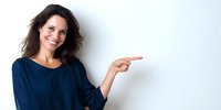 Smiling woman with wavy brown hair in navy blue top pointing to the right against white background, ideal for business presentations or advertising.