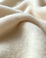 Soft cream colored wool textile macro shot showing natural fiber texture and gentle folds creating subtle shadows and highlights. Suitable for luxury fashion backgrounds.