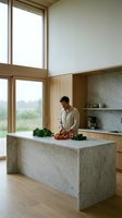 Modern kitchen interior with young Caucasian man preparing fresh vegetables on marble island. Contemporary home design with wooden elements and large windows.