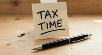 Yellow sticky note with TAX TIME text and black pen on wooden desk surface for accounting and financial planning reminders during tax season preparation.
