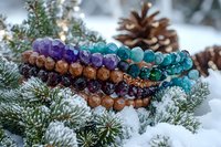 Colorful crystal bracelets with amethyst, turquoise and brown beads arranged on snowy pine branches with pinecone, winter holiday spiritual jewelry composition.