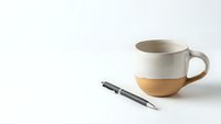 Modern ceramic coffee mug with terracotta base and sleek pen on clean white background for minimalist workspace design and branding projects.