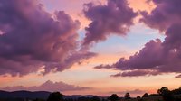 Dramatic purple and pink sunset sky with fluffy clouds over mountain silhouette landscape creating romantic evening atmosphere for nature backgrounds.