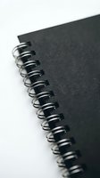 Spiral-bound notebook with black cover and metal wire binding detail against white background, suitable for stationery, office supplies, education, and business organization concepts.